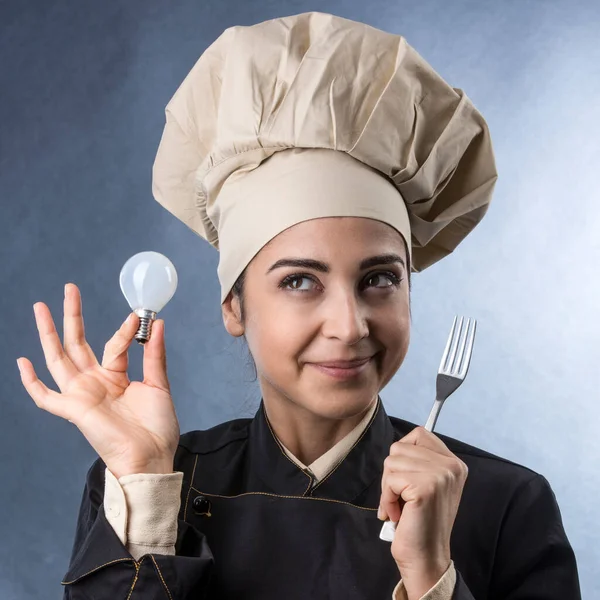 シェフの制服を着たシェフの女性は電球を手に持っている創造的なレシピのための良いアイデアを見つけることを意味します — ストック写真