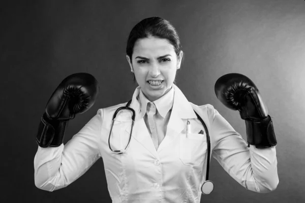 白いコートとボクシングの手袋の女性医師は 灰色の背景に隔離され あきらめたくない人の表情を持っています — ストック写真