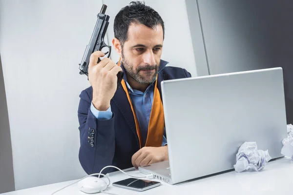 彼のオフィスに座って 彼の手に銃を持っている彼のコンピュータで憎しみで見て — ストック写真
