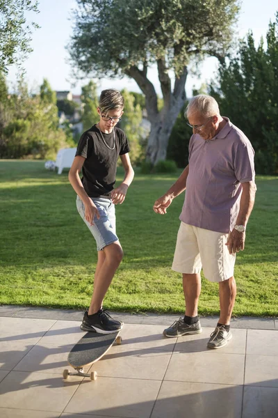 Teenage Vnuk Učí Svého Staršího Dědečka Zahradě Jezdit Skateboardu — Stock fotografie