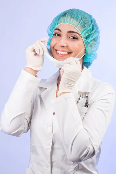 身穿白衣 头戴绿帽 头戴乳胶手套的女医生决心要戴上白色的面罩 露出美丽的笑容 与白色背景隔离在一起 — 图库照片