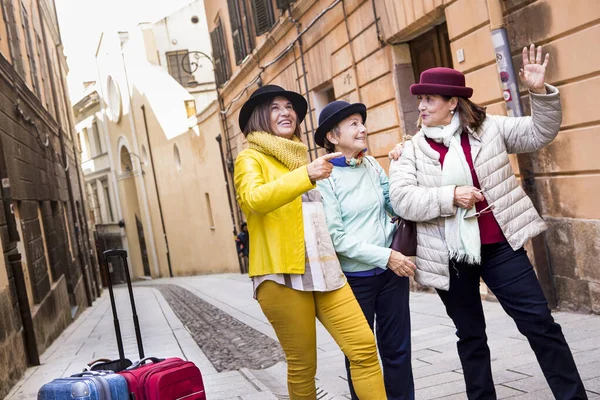 带着帽子和彩色衣服的老年游客们带着手提箱在城市里游玩 — 图库照片