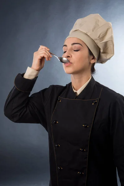 女厨师从勺子里尝一道菜 用灰色背景隔开 — 图库照片