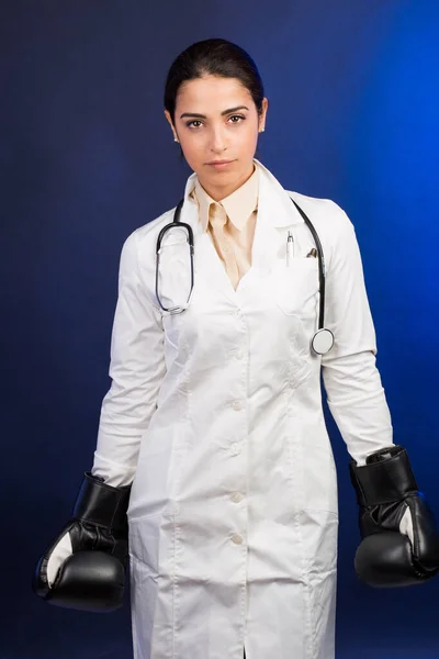 白いコートとボクシングの手袋の女性医師青の背景に隔離され あきらめたくない人の表情を持っています — ストック写真