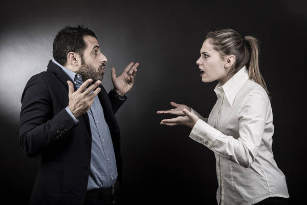 темноволосый мужчина в тёмной куртке и синей рубашке защищает себя от нападений своей блондинки-подружки, изолированной на чёрном фоне