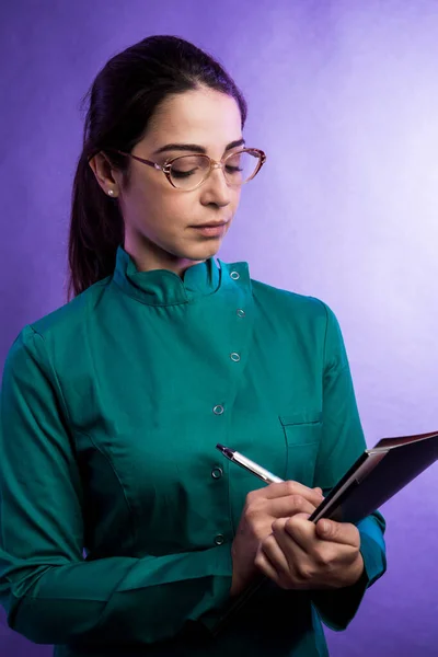 严重的女医生在眼镜文件夹与医疗报告和笔 隔离蓝色背景 — 图库照片