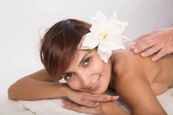 stock image beautiful woman with bob hair and a lotus flower on her head relaxes on a spa bed lying on her stomach ready to receive a back massage