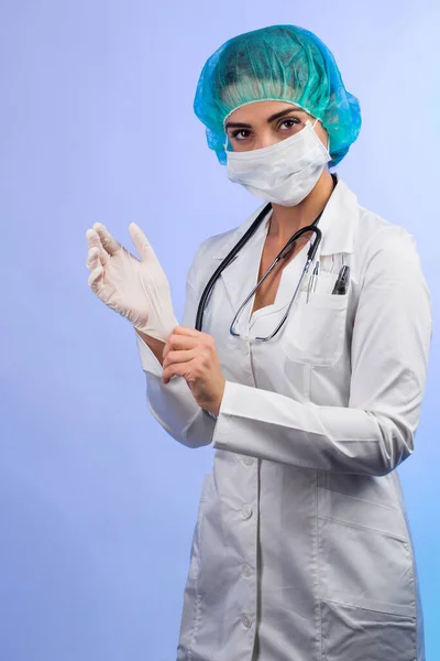 身穿白衣 戴白色面罩 头戴绿色帽子的女医生决心戴上乳胶手套 与白色背景隔离 — 图库照片