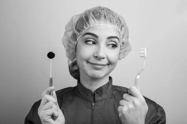 Zahnarzt Mit Mütze Und Kittel Blickt Auf Zahnbürste Und Zahnspiegel — Stockfoto