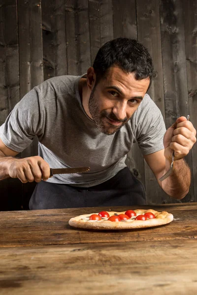 髭を生やした黒髪の男は 木の背景に隔離されたチェリートマトとピザを食べることになっています — ストック写真