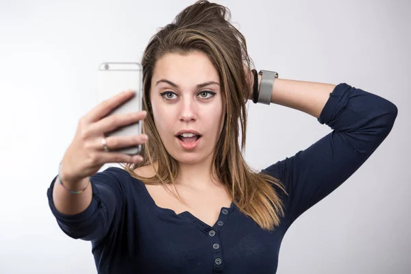 stock image Beautiful blonde girl in blue dress, takes a selfie with very confident expression with her mouth open - light background