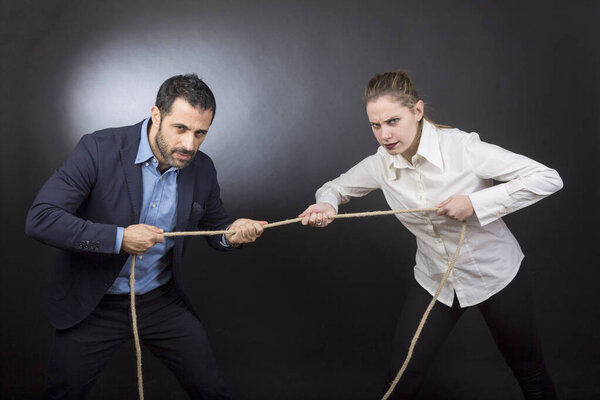 Мужчина в куртке перетягивает канат против блондинки. Каждый из них стремится одержать верх над другим. Изолированный на черном фоне