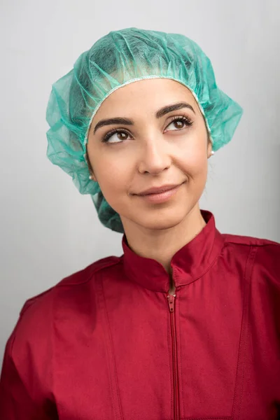 灰色の背景にアマランスコートと緑の帽子を持つ女性医師の肖像画 — ストック写真
