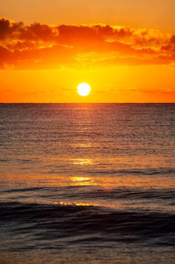 Koyu sarı gökyüzü ile denizin üzerinde gün batımı