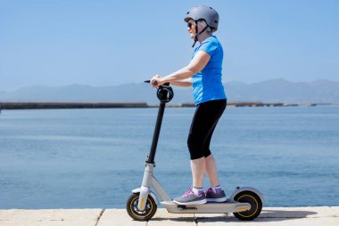 Kadın turist denizin önünde elektrikli scooter kullanıyor.