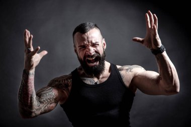 Siyah arka planda dövmeleri olan yakışıklı sakallı bir adamın portresi.