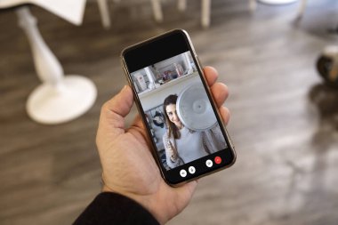 Cep telefonu bağlantısını tutan bir adamın detayları. Ekranda uzaktan yemek pişiren ve şaka yapan bir kızın görüntüsü var.