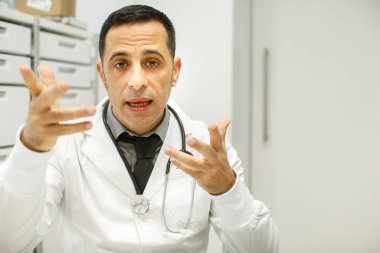 Siyah saçlı, beyaz önlüklü bir doktor ofisinde hareketli bir şekilde oturuyor.