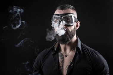 Siyah arka planda dövmeleri olan yakışıklı sakallı bir adamın portresi.