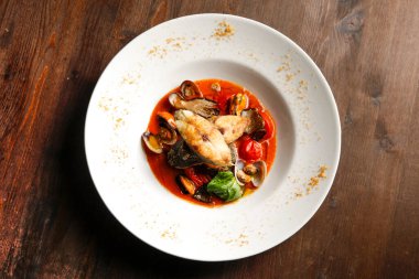 Beyaz tabakta domates ve biber soslu balık, ahşap arka planda, yakın plan. 