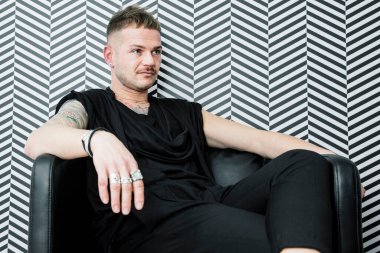 Cagliari, İtalya - 03-20-2018: Siyah dövmeli sarışın beyaz adam ve çizgili arka planda bir koltukta dinleniyor