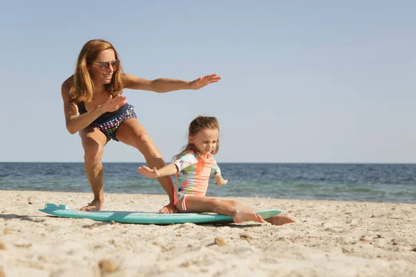 身着游泳衣的母亲在海滨向女儿传授冲浪的基本知识 — 图库照片