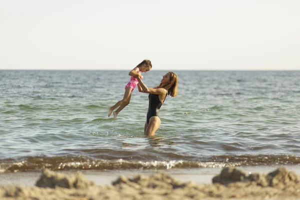 水着姿のお母さんと娘が遊びながら海で泳いでいます — ストック写真
