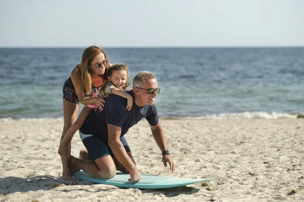 由父亲 母亲和女儿组成的快乐的家庭与海滩上的冲浪板一起玩得很开心 — 图库照片
