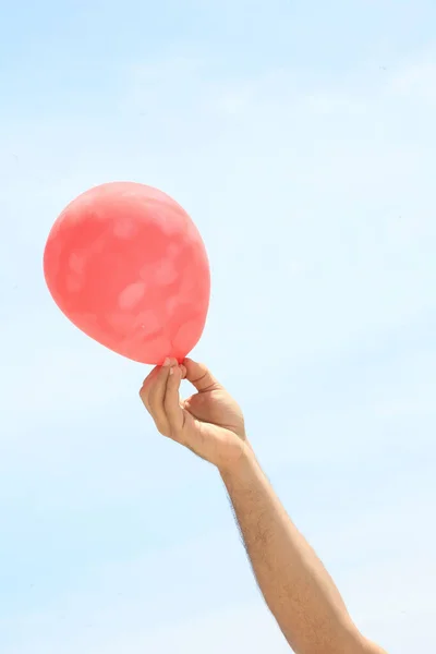 一个在蓝天背景上拿着一个彩色气球的年轻人的手 — 图库照片