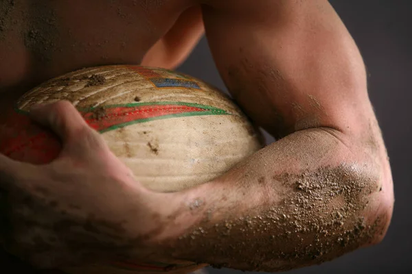 close up of muscular young man playing with rugby ball against black background