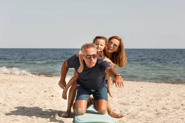 由父亲 母亲和女儿组成的快乐的家庭与海滩上的冲浪板一起玩得很开心 — 图库照片
