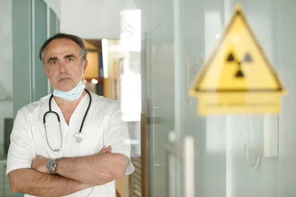 Fifty-year-old doctor in a white coat and a lowered surgical mask, looks seriously from a hospital room