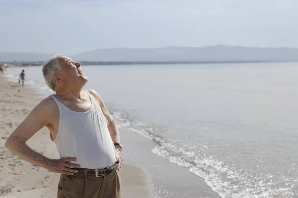 海のそばのタンクトップに身を包んだ年配の紳士が真剣な表情で立っている — ストック写真