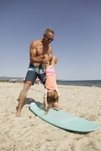 爸爸戴着太阳镜 穿着泳衣 在海滨向女儿传授冲浪的基本知识 — 图库照片