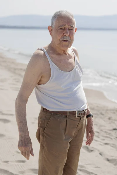海のそばのタンクトップに身を包んだ年配の紳士が真剣な表情で立っている — ストック写真