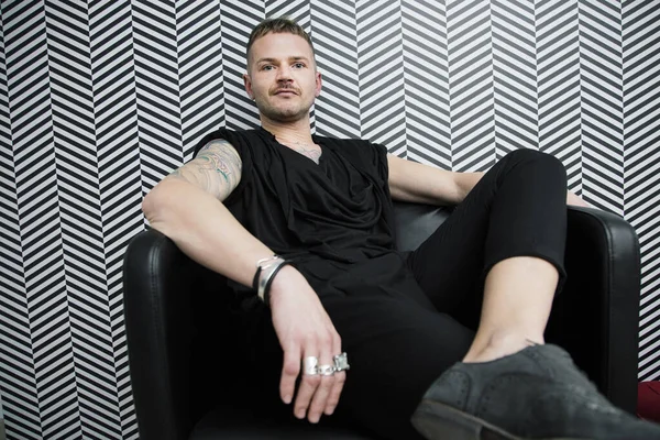 Blond Biały Mężczyzna Tatuażami Ubrany Czarno Siedzi Relaksujący Fotelu Tle — Zdjęcie stockowe