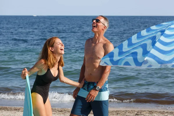 夫妇与冲浪板放松和笑在海滩附近的伞 — 图库照片