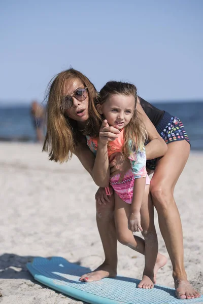 身着游泳衣的母亲在海滨向女儿传授冲浪的基本知识 — 图库照片