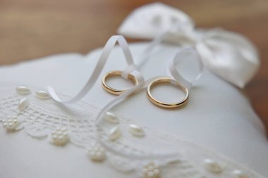 Masanın üzerinde beyaz bir yastık ve bir buket çiçekle alyanslar. 