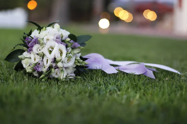一束缀着白花和紫罗兰玫瑰的新娘花束躺在草坪上 — 图库照片