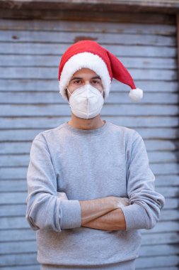 Noel Baba şapkalı ve maskeli genç adam duvarın yanında duruyor.
