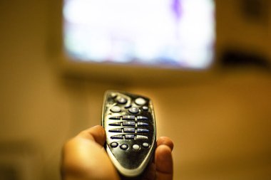 Arka planda bir el ve bulanık bir televizyon tarafından tutulan ön planda uzaktan kumanda
