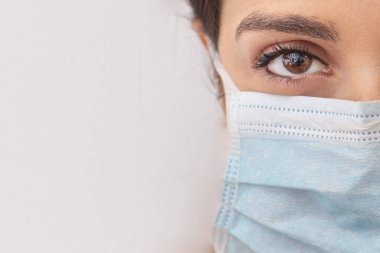 Beyaz tişörtlü esmer kız beyaz arka planda izole edilmiş cerrahi bir yüz maskesi takıyor.