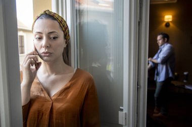 Pencerenin önünde oturan üzgün yüzlü genç bir kadın başka tarafa bakıyor.