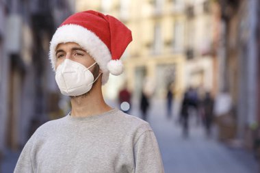 Koruyucu maskeli ve Noel Baba şapkalı bir adam dışarıda bekliyor.