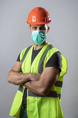 Sarı koruyucu kask yeleği ve cerrahi maskeli işçi, gri arka planda izole edilmiş.