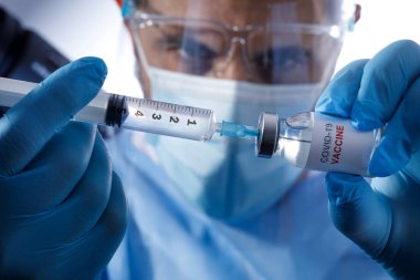 Cerrahi maskeli ve lateks eldivenli bir doktor beyaz arka planda izole edilmiş cam şişeden anti-covid aşıyı aldı.