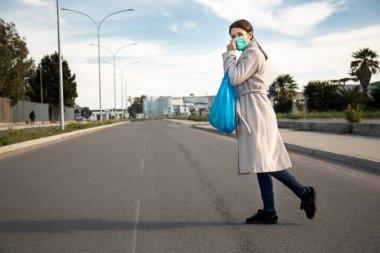Kadın elinde mavi bir çantayla karşıdan karşıya geçiyor.