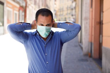 man with blue shirt adjusts a stationary face mask standing in the city center clipart