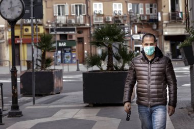 Koyu renk ceketli, traşlı adam şehir ortamında yürürken koruyucu bir maske takıyor.
